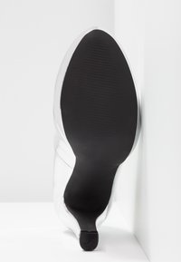 Srebrny but na wysokim obcasie o błyszczące wykończeniu, spiczastym nosku i czarnej gumowej podeszwie. Podeszwa ma poziome rowki dla lepszej przyczepności.