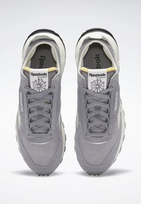 Paire de baskets Reebok Classic grises avec tiges en mesh et en daim, semelles intermédiaires blanches et accents jaunes sur la languette, vues de dessus.
