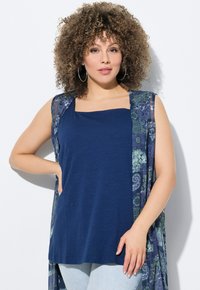 Top senza maniche blu navy con scollatura quadrata, indossato sotto un cardigan trasparente aperto con stampa floreale nelle tonalità di blu e verde.