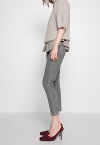 Pull en maille gris clair superposé sur une blouse à rayures noire et blanche, associé à un jean gris foncé et des talons bordeaux texturés avec un stiletto.