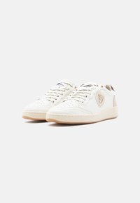 Λευκά δερμάτινα αθλητικά παπούτσια με διάτρητες μύτες, στρογγυλά κορδόνια, μπεζ λεπτομέρειες, λαστιχένιες σόλες και λογότυπο στη μία πλευρά.