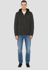 Sweat à capuche zippé en maille gris fonc é avec texture côtelée, capuche avec cordon de serrage et poches avant, associé à un jean bleu clair et des baskets noires.