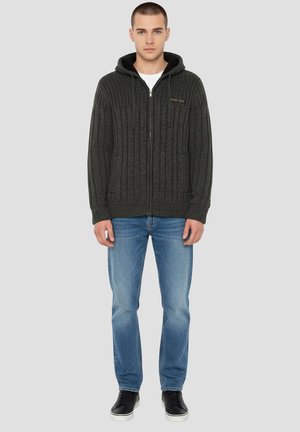 Mørkegrå strikket hættejakke med lynlås, ribstrikket struktur, snor i hætten og forlommer, kombineret med lyseblå jeans og sorte sneakers.