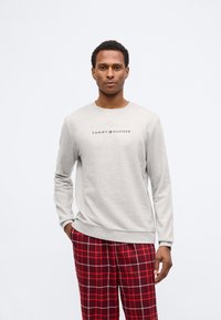 Sweatshirt gri deschis cu guler tip crew și logo-ul 'TOMMY HILFIGER' pe piept, asortat cu pantaloni de pijama în carouri roșii cu accente gri.