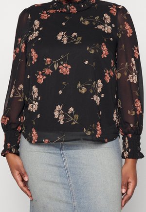 Schwarze, transparente Bluse mit rosa- und beigen Blumenmuster, hohem Rüschenkragen, gerafften langen Puffärmeln mit elastischen Bündchen, kombiniert mit hellem Jeansrock.