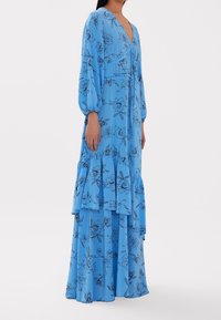 Robe maxi bleue à motif floral avec de longues manches bouffantes, un col en V et des volants superposés à l'ourlet, fabriquée en tissu léger.