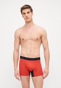 Red boxer briefs with black waistband featuring "PUMA" logo, made from a smooth, elastic material, highlighting a fitted design.