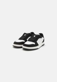 Czarno-białe sneakersy z połączeniem gładkiej i zamszowej faktury, okrągłym noskiem, grubą gumową podeszwą oraz tradycyjnym sznurowanym zapięciem.