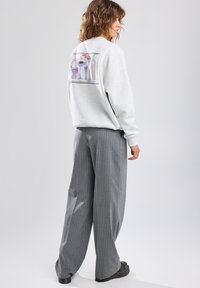 Light gray sweatshirt with graphic design on the back, paired with gray pinstriped wide-leg pants and black platform shoes.