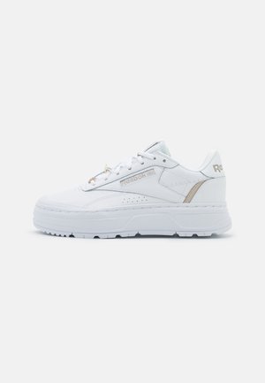 Baskets Reebok basses blanches à semelle épaisse, lacets à l'avant, avec des accents beiges sur le côté et le talon sur un fond uni.