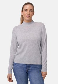 Lichtgrijze longsleeve trui met een hoge kraag, gemaakt van zachte stof, met ribgebreide boorden en zoom, gedragen met blauwe jeans.