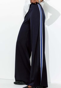 Pantalons larges navy en tissu doux avec des rayures verticales blanches et bleues sur les côtés, dotés d'une taille élastique.