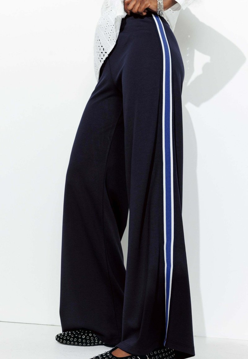Pantalons larges navy en tissu doux avec des rayures verticales blanches et bleues sur les côtés, dotés d'une taille élastique.