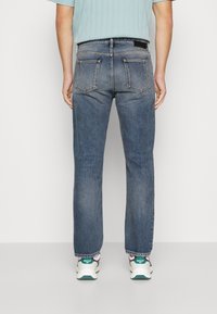 Jeans di denim azzurro chiaro con un taglio dritto, dotati di due tasche posteriori e un'etichetta nera in vita. Abbinati a sneakers multicolori.