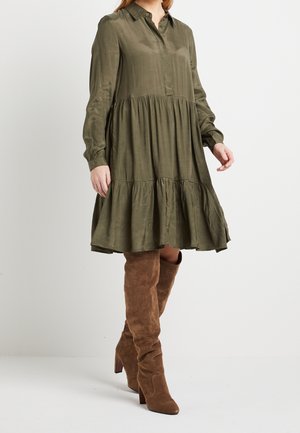 Olivgrünes, langärmliges Hemdkleid mit Knopfleiste, gerafftem, mehrstufigem Rock, weicher Textur, kombiniert mit braunen, kniehohen Wildlederstiefeln.