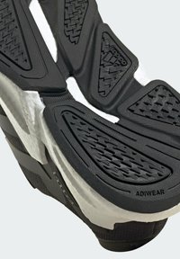 Suela de zapatilla en blanco y negro con goma texturizada para mayor agarre. Presenta patrones en zigzag y hexagonales, con la marca "ADIWEAR".