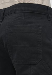 Mustad lõuendpüksid keskmise vöökohaga, millel on tagataskul topeltõmblus ja tekstureeritud kanga välimus.