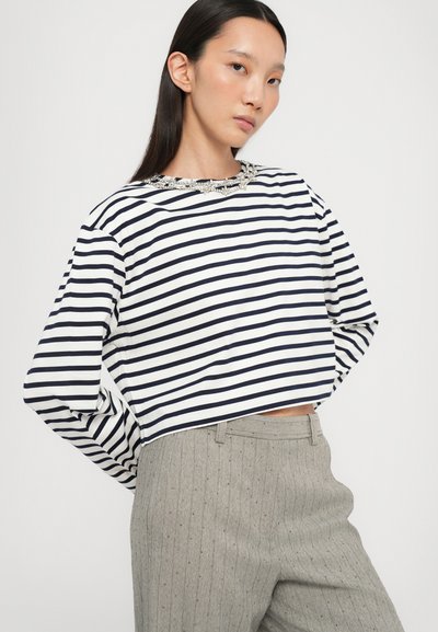 Striped long-sleeve crop top in navy and white with a beaded neckline, paired with gray pinstriped pants featuring subtle texture and detail.