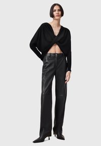 Black cropped sweater with a twisted design, paired with high-waisted black leather pants and pointed toe heels. Smooth texture and fitted silhouette.