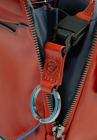 Bolso de cuero rojo con cremallera de acento azul y un accesorio de llavero de metal. Presenta una textura suave y un forro interior azul contrastante.