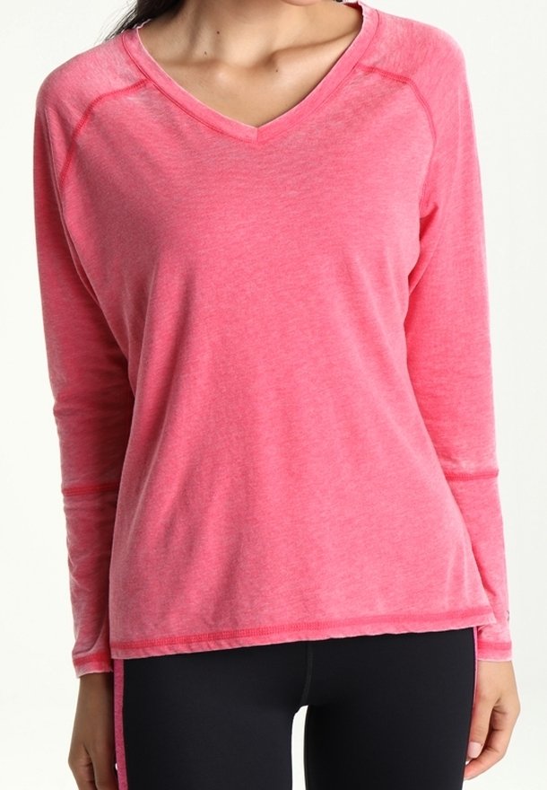 Lange mouwen, zachtroze V-hals shirt met raglanmouwen, met een ontspannen pasvorm en subtiele textuur. Gecombineerd met zwarte leggings.