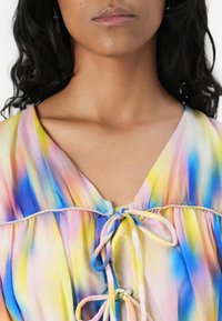 Bunte, leichte Bluse mit V-Ausschnitt, Bindedetail in der Mitte und fließendem Stoff mit einem Farbverlauf aus Pink, Blau und Gelb.