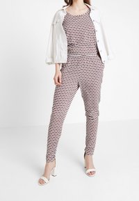 Tvådelad outfit bestående av en mönstrad linne och slim-fit byxor i vinröd med vita detaljer. Matchas med en vit denimjacka och klackar.