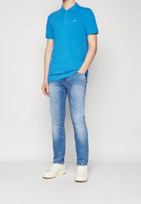 Lyhythihainen kirkkaan sininen polopaita, puuvillamateriaalia, kauluksella ja logolla. Yhdistetty vaaleansinisiin slim-fit-farkkuihin ja valkoisiin lenkkareihin.