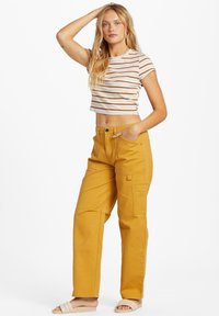 Randig, kortärmad t-shirt i vitt, orange och brunt. Gula cargobyxor med framfickor och avslappnad passform. Platta sandaler.