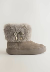 Bruine suède enkellaars met een nepbont manchette, voorzien van een strik met gouden accenten. Dikke rubberen zool voor comfort en stabiliteit.