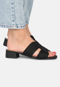 Sandales à glissière tissées noires avec un petit talon bloc, présentant deux brides croisées et des semelles en cuir lisse. Fini poli et design neutre.