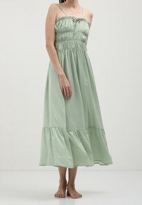 Robe vert clair, longueur genoux, avec bretelles spaghetti réglables, corsage froncé et ourlet à volants superposés. Tissu doux et texturé.