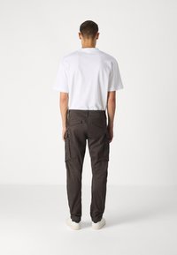 Pánský outfit s jednoduchým bílým tričkem a tmavými cargo kalhotami s bočními kapsami, doplněný světle zbarvenými teniskami. Minimalistický design.