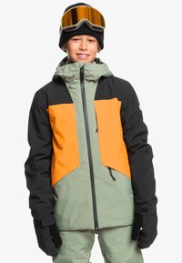 Skijacke in Grün, Schwarz und Orange. Hat einen hohen Kragen, einen Frontreißverschluss und elastische Bündchen. Ausgestattet mit einer Kapuze und Taschen.