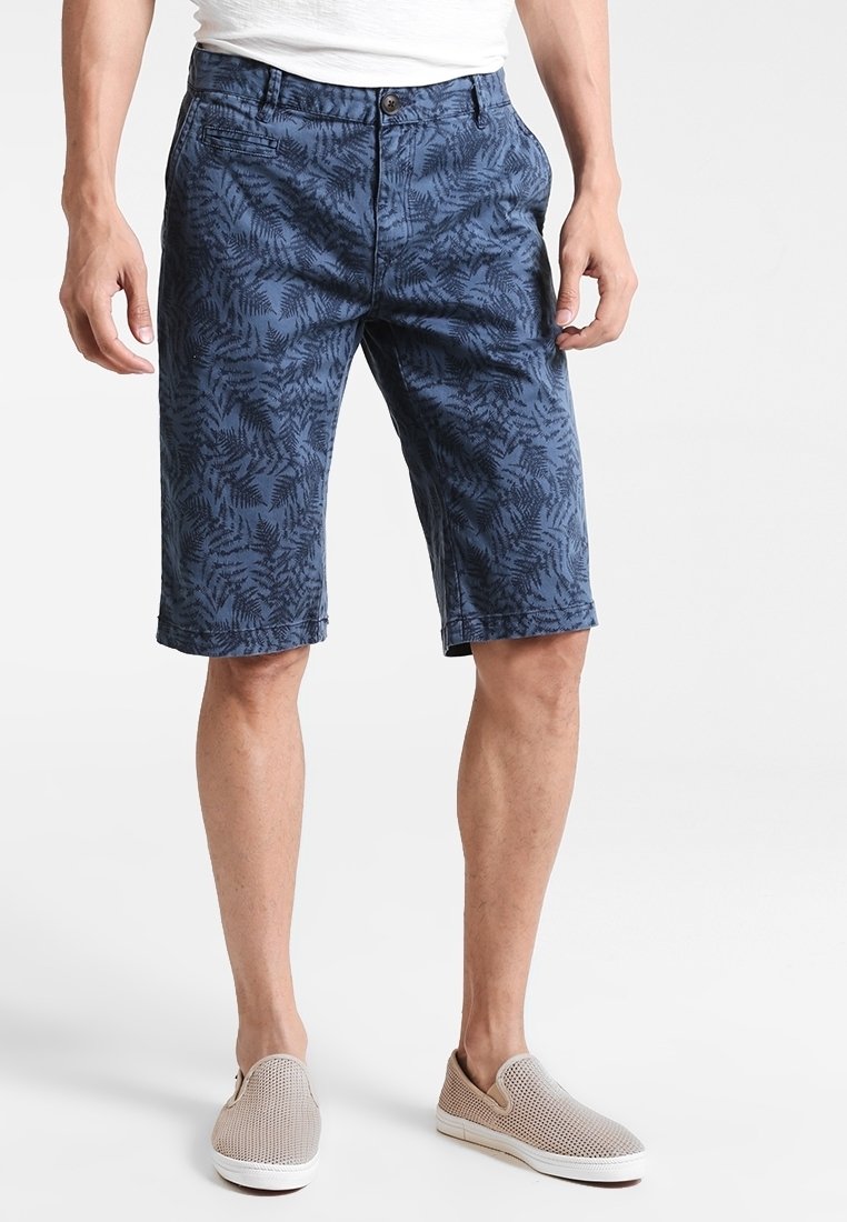 Marinblå shorts med ett mönster av ormbunksblad, tillverkade av lätt tyg. Utrustade med knappstängning och bälteshällor, som slutar strax över knäet.