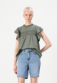 Grøn mønstret bluse med flæser på ærmerne og samlede detaljer, parret med høj talje denimshorts i lyseblå.