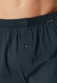 Boxers en coton bleu marine avec une taille élastique, dotés d'une fermeture à boutons à l'avant et d'une poche plaquée. Texture douce, design décontracté.