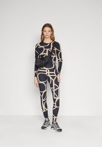 Marine aktivt treningstøy sett med beige geometrisk mønster; tettsittende topp og leggings; kombinert med en svart crossover-veske og grå treningssko.
