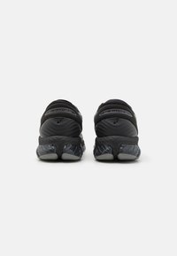 Black athletic shoes with a textured upper, featuring a padded collar and a glossy, patterned midsole. The outsole is gray and flexible.