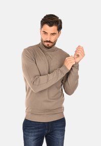 Maglione a collo alto marrone in tessuto a maglia liscia. Presenta un design aderente, polsini e orlo a costine. Abbinato a jeans blu scuro.