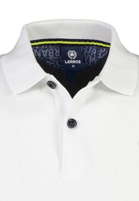 Weißes Polohemd aus strukturiertem Stoff, mit zwei schwarzen Knöpfen am Kragen und einem dunkelblauen, gemusterten Innenkragen, der mit einer grünen Akzentlinie versehen ist.