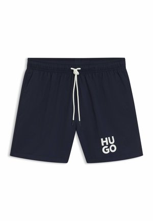 Shorts de bain navy avec une taille élastique, un cordon blanc et un grand logo "HUGO" blanc en bas à gauche. Texture de tissu lisse.