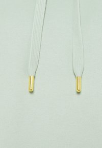 Tela de sudadera con capucha en verde menta con una textura suave, que presenta dos cordones con extremos de metal dorado. Diseño simple, sin patrones ni adornos.