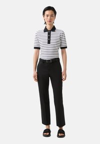 Polo rayé noir et blanc, avec un col noir et une patte de boutonnage, associé à un pantalon noir ajusté et des sandales noires.
