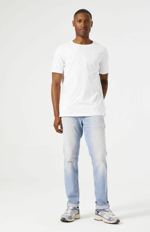 White cotton t-shirt with short sleeves, paired with light blue jeans and gray sneakers. Simple design, casual fit, and minimal detailing.
