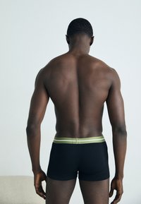 Boxer da uomo neri con una cintura a righe verdi e bianche, realizzati in tessuto morbido, che presentano una sagoma aderente e un design minimalista.