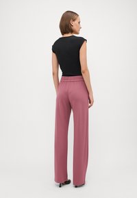 Zwarte, aansluitende top met korte mouwen, gecombineerd met roze wijde broeken met een elastische tailleband en een soepele textuur. Zwarte hakken.