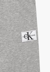 Ljust grått tyg med en vit rektangulär lapp sydd på, som visar svarta "cK"-bokstäver och texten "Calvin Klein Jeans".