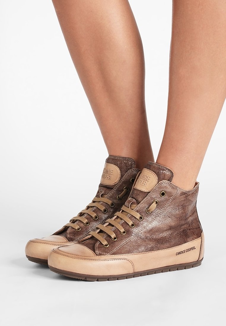 Baskets montantes en cuir marron avec bouts d'orteils, lacets et semelles beige, portées pieds nus sur fond blanc.