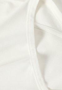 Gros plan d'un tissu blanc avec des coutures pliées visibles et des détails de couture fins sur une surface textile lisse.